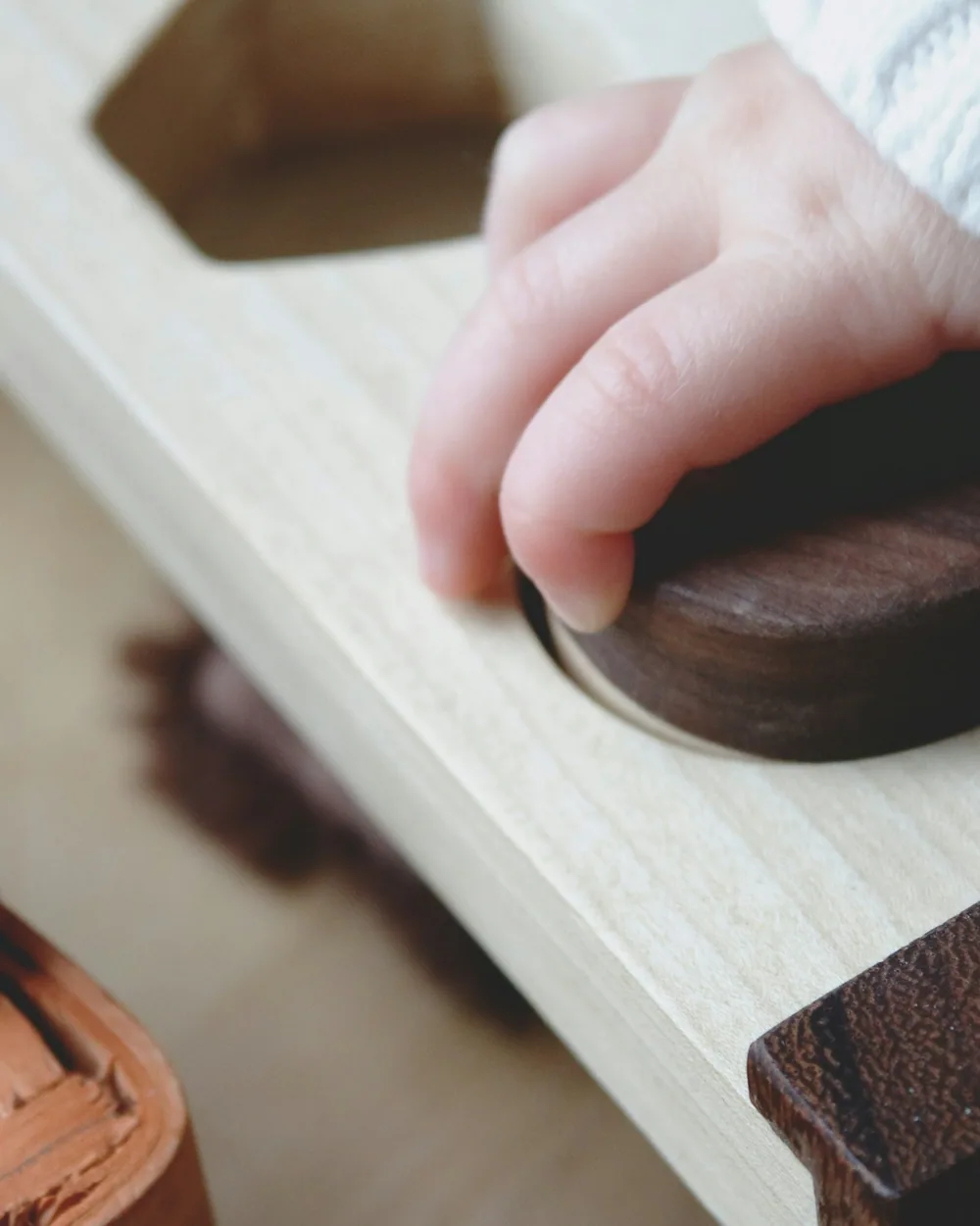 A child's hand setting a smooth wooden disc down on the edge of a table